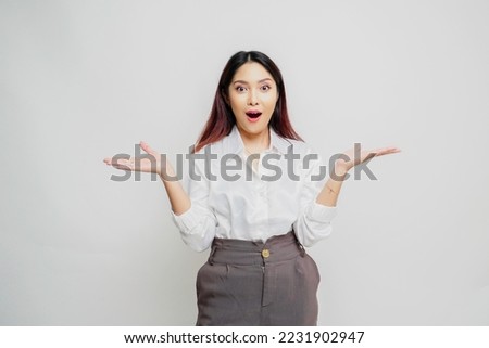 Shocked Asian woman wearing white shirt pointing at the copy space beside her, isolated by white background