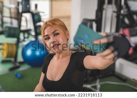 A happy asian woman taking an angled selfie of herself during a training at the gym. Posting a workout photo to her social media.