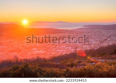 Beautiful morning cityscape. View from the mountain to the city at sunrise. The sun rises over the sea bay and mountains. Travel and tourism in the Magadan region. City of Magadan, Far East of Russia. Royalty-Free Stock Photo #2231924453
