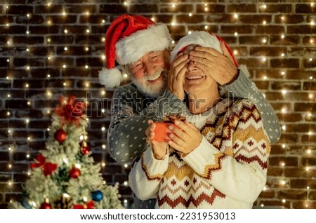 Surprise for her. Christmas event and celebration. Happy Senior couple with Santa hats exchange a present