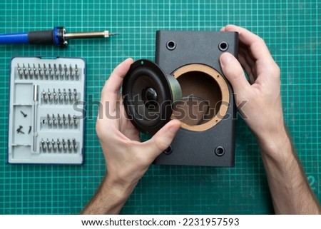 Man repairs an audio speaker. Workplace with a screwdriver and a polarizer. Master is holding a music speaker. Top view