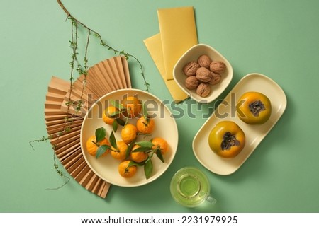 Set up New year table with fruits, nut and tea. Paper fans, lucky money,  branches flower on green background. New year decoration idea. 