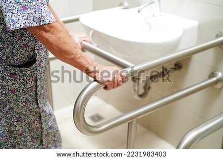 Asian elderly old woman patient use toilet support rail in bathroom, handrail safety grab bar, security in nursing hospital. Royalty-Free Stock Photo #2231983403