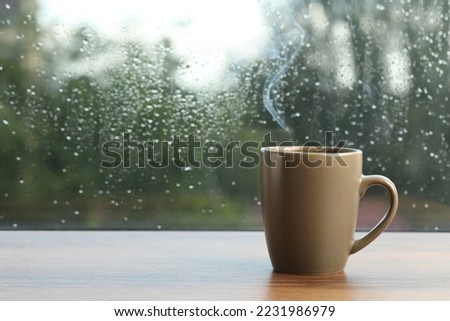 Cup of hot drink near window on rainy day. Space for text
