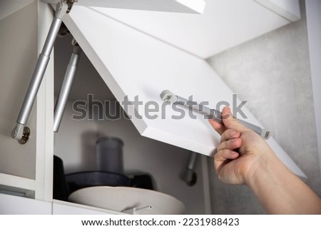 A furniture assembly worker holds a retractable gas spring to open and support a cabinet door. Modern furniture fittings Royalty-Free Stock Photo #2231988423