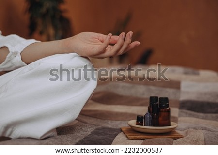 Crop woman with mudra hand doing yoga on bed with essential oils for aromatherapy at home 