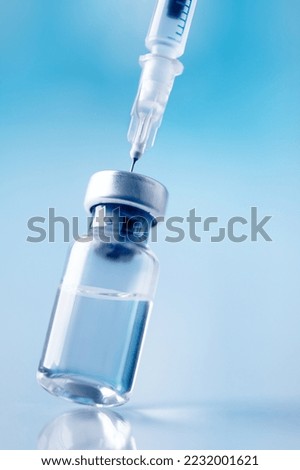 Glass vial and syringe with injection over blue background. Vaccination or beauty therapy concept. Royalty-Free Stock Photo #2232001621