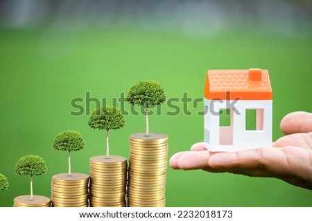 Rising house prices idea concept. Trees and top house model on stacked coins against green background. Real estate and money affairs. Someone who dreams of buying a new home. Post-Production Technique