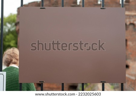 A template with a blank dark sign hanging on a fence of metal bars. Background for inscriptions.