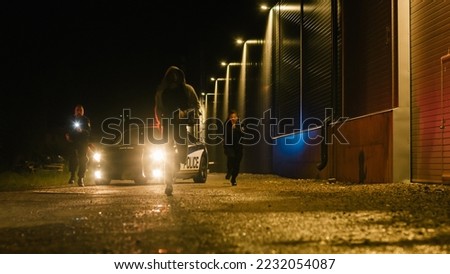 Two Police Officers in Pursuit of a Suspect. Cops Getting out of the Car Start Chasing Criminal on Foot Through the Dark City Streets. Heroic Officers Catching and Arresting Drug Dealer, Murdered Royalty-Free Stock Photo #2232054087