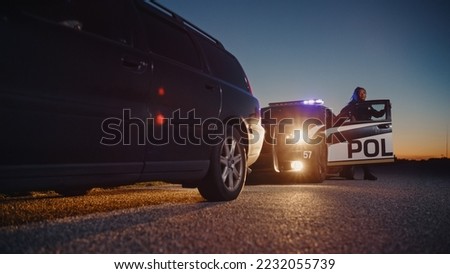 Black Female Police Officer Stepping Out of Patrol Car and Heading Towards a Pulled over Car. Cops Responding to a 911 Call About a Suspicious Car Stopped on the Road, Investigating the Situation Royalty-Free Stock Photo #2232055739