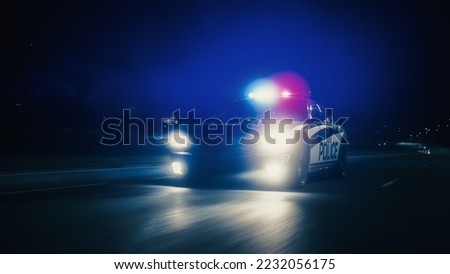 Traffic Patrol Car In Pursuit, Driving Fast with Sirens Blazing through the City Streets. Officers of the Law Chasing a Suspect. Cops in Squad Car React to Emergency Call. Cinematic Night Shot Royalty-Free Stock Photo #2232056175
