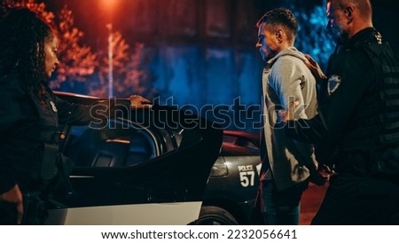 Two Police Officers Arrest Suspect, Put Him in Patrol Сar. Officers of the Law Handcuff Dangerous Criminal on Dark City Street. Cops Arresting Felon, Fight Crime. Cinematic Documentary Royalty-Free Stock Photo #2232056641