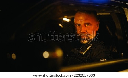 Portrait of Police Officer Sitting in the Patrol Car, Looking at the Camera. Officer of the Law Maintains Public Order and Safety, Prevents and Investigates Criminal Activity, Helps and Saves People