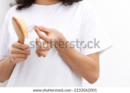 a close horizontal photo of women's hands cleaning a wooden massage comb from fallen hair, standing in a white T-shirt on a white background