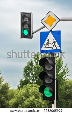 Post with Priority Road and Pedestrian crossing signs near traffic lights outdoors