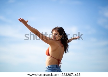 Rear view portrait of beautiful young woman standing with hands outstretched against sky looking back at camera