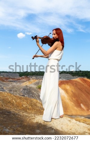 Close-up adult caucasian woman violinist playing violin on summer lavender field, romantic musician in blue dress enjoying walking on nature, back view