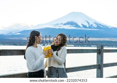 Happy Asian woman travel Japan on autumn holiday vacation. Attractive girl friends enjoy and fun outdoor lifestyle travel the lake around Mt Fuji covered in snow and looking beautiful nature together.