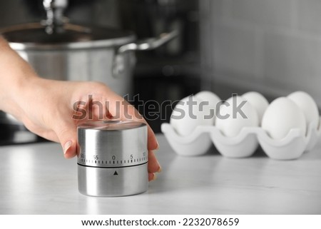 Woman winding up kitchen timer at white table indoors, closeup. Space for text Royalty-Free Stock Photo #2232078659