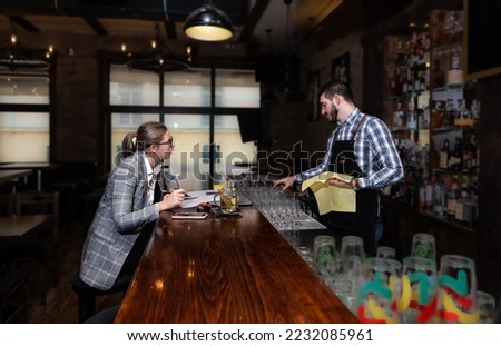 Young lonely business woman sitting at the bar wooden counter working and talking with the bartender. Customer chatting with employee at the cafeteria. Royalty-Free Stock Photo #2232085961