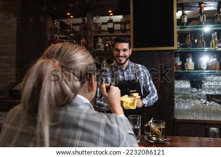 Young lonely business woman sitting at the bar wooden counter working and talking with the bartender. Customer chatting with employee at the cafeteria. Royalty-Free Stock Photo #2232086121