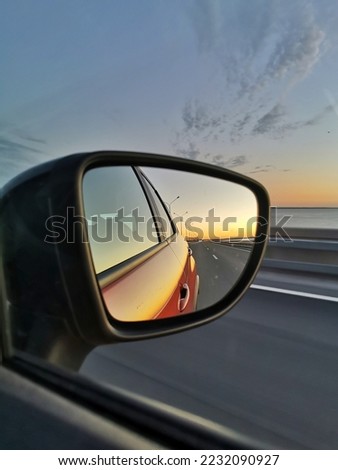 Reflection of road and sunset in the side mirror of the orange car. Concept of road trip and traveling by car.  Royalty-Free Stock Photo #2232090927