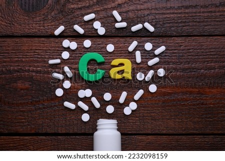Paper symbol Ca (Calcium), medical bottle and pills on wooden table, top view