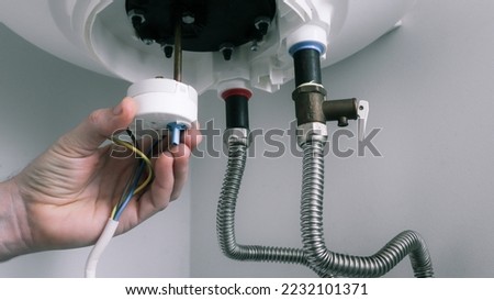 The hand of a plumber installs a thermostat in a boiler after repair. Water heater repair. Royalty-Free Stock Photo #2232101371