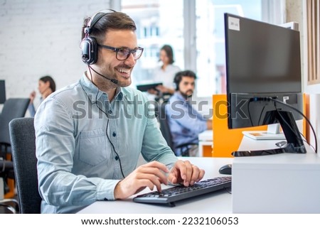 Young male technical support dispatcher in call center. Man in call center with headset helping customer. Royalty-Free Stock Photo #2232106053