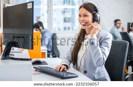 Friendly female helpline operator in call center. Young woman working in call center and holding microphone on headset with hand. Royalty-Free Stock Photo #2232106057