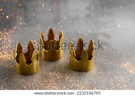 Epiphany  Day or Dia de Reyes Magos concept. Three gold crowns on black background with golden particles. Royalty-Free Stock Photo #2232106705
