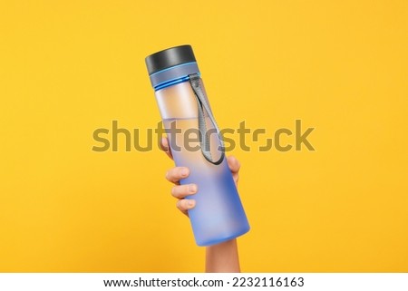 Woman holding bottle of drink on orange background, closeup Royalty-Free Stock Photo #2232116163