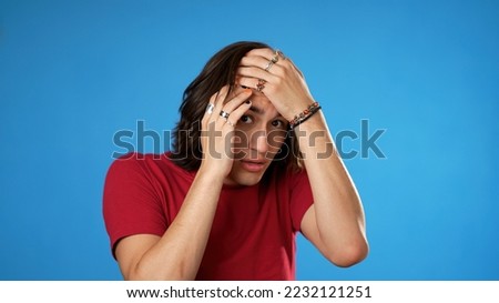 Shocked surprised portrait of angry, frustrated upset Hispanic Latino man covers eyes with hands isolated on solid blue background.