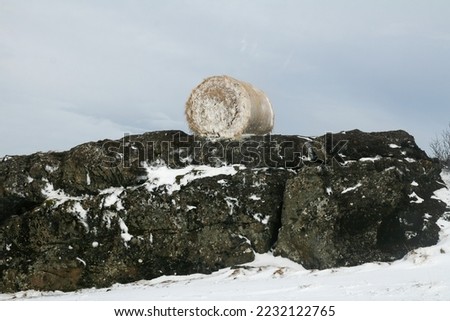 A haystack roll covered in snow laying on rocks in Icelandic contryside by winter