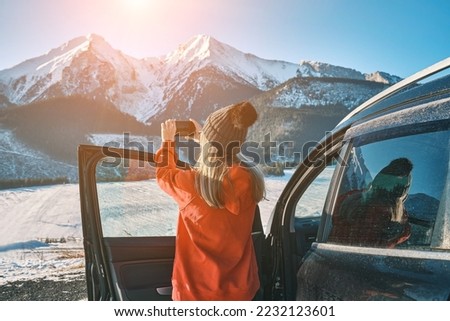 Woman travel exploring, enjoying the view of the mountains, landscape, lifestyle concept winter vacation outdoors.
Female with mobile phone standing near the car in sunny day.