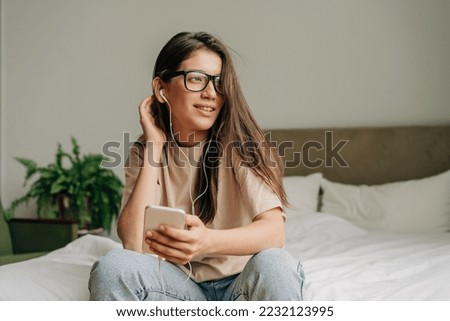 A young adolescent girl uses a phone and headphones to listen to music. Royalty-Free Stock Photo #2232123995