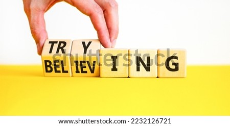Trying and believing symbol. Businessman turns wooden cubes and changes the word Believing to Trying. Beautiful yellow table white background, copy space. Business, trying and believing concept.
