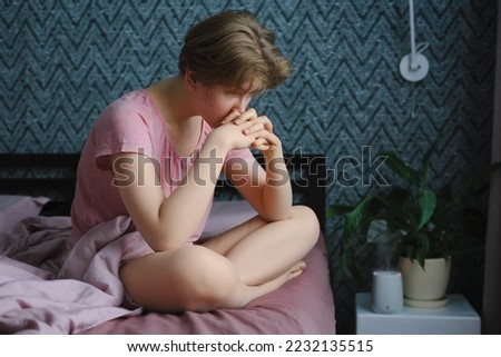 Young girl sits cross-legged on the bed and is sad. Problems of adolescence Royalty-Free Stock Photo #2232135515