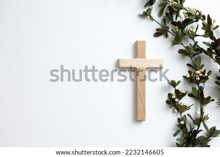 Simple wood cross and border of branches with white berries on a white background with copy space