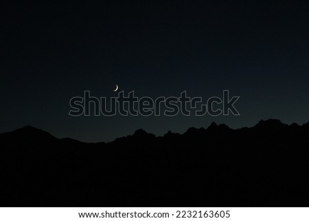 Crescent moon over the Swiss Alps. Late twilight dusk shot of moon over silhouetted mountains (Verbier, Valais, Switzerland)