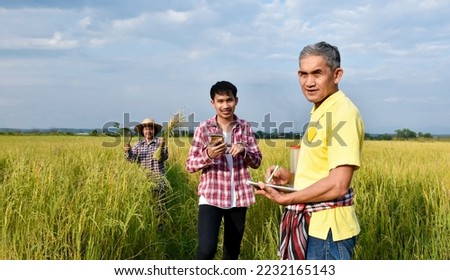Portrait asian elderly man in yellow shirt is taking note planting information by asking and interviewing young asian man and female farmer nearby, soft and selective focus.