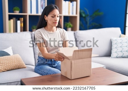 Young hispanic woman opening cardboard box skeptic and nervous, frowning upset because of problem. negative person. 