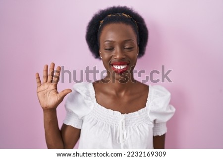 African woman with curly hair standing over pink background showing and pointing up with fingers number five while smiling confident and happy. 