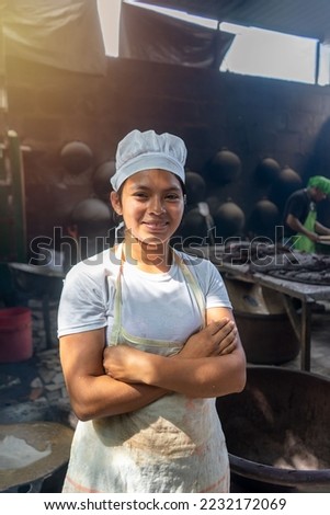 Vertical photo of a Young Latina woman from Nicaragua dressed in her cook uniform in a kitchen with traditional Latin American stoves and comales Royalty-Free Stock Photo #2232172069