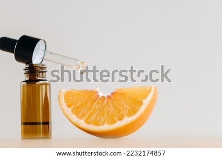 Essential oil in one bottle and a piece of orange standing on the surface.
