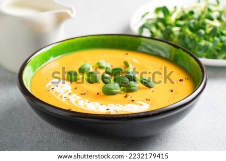 Pumpkin fall soup in green bowl on the light gray table. Butternut squash cream soup garnished with heavy cream and fresh sunflower microgreen. Selective focus Royalty-Free Stock Photo #2232179415