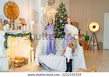 two girls and a little boyhave fun and play with pillows in a room with Christmas decor. sisters and younger brother. a close-knit family. the concept of the New Year holidays. happy childhood.