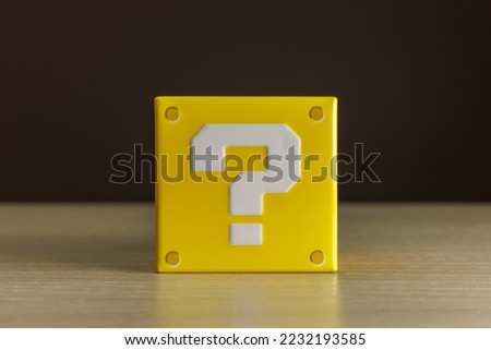 Indoor still-life photo of a little yellow box with a big white question mark printed on each face. It recalls a graphic element of a famous platform video game. Royalty-Free Stock Photo #2232193585