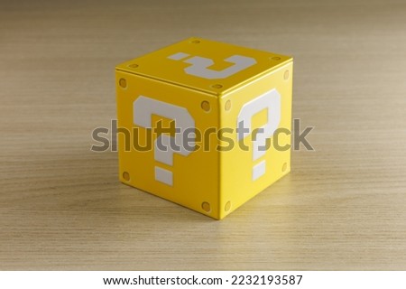 Indoor still-life photo of a little yellow box with a big white question mark printed on each face. It recalls a graphic element of a famous platform video game. Royalty-Free Stock Photo #2232193587